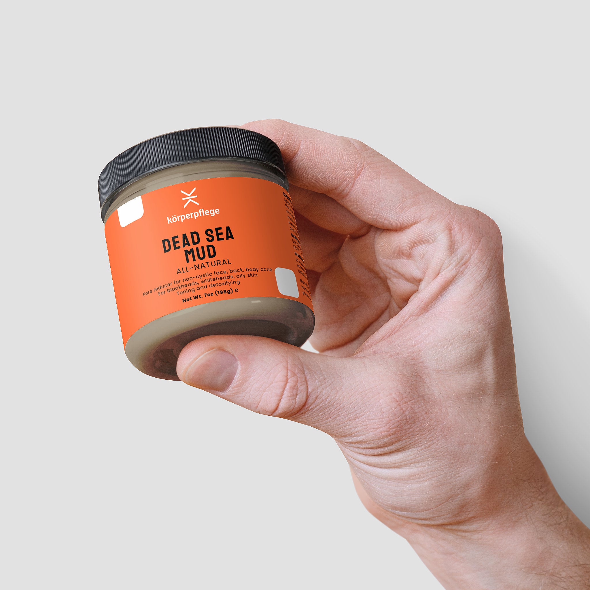 Hand holding a jar of Körperpflege's Dead Sea Mud Mask on a light gray background.